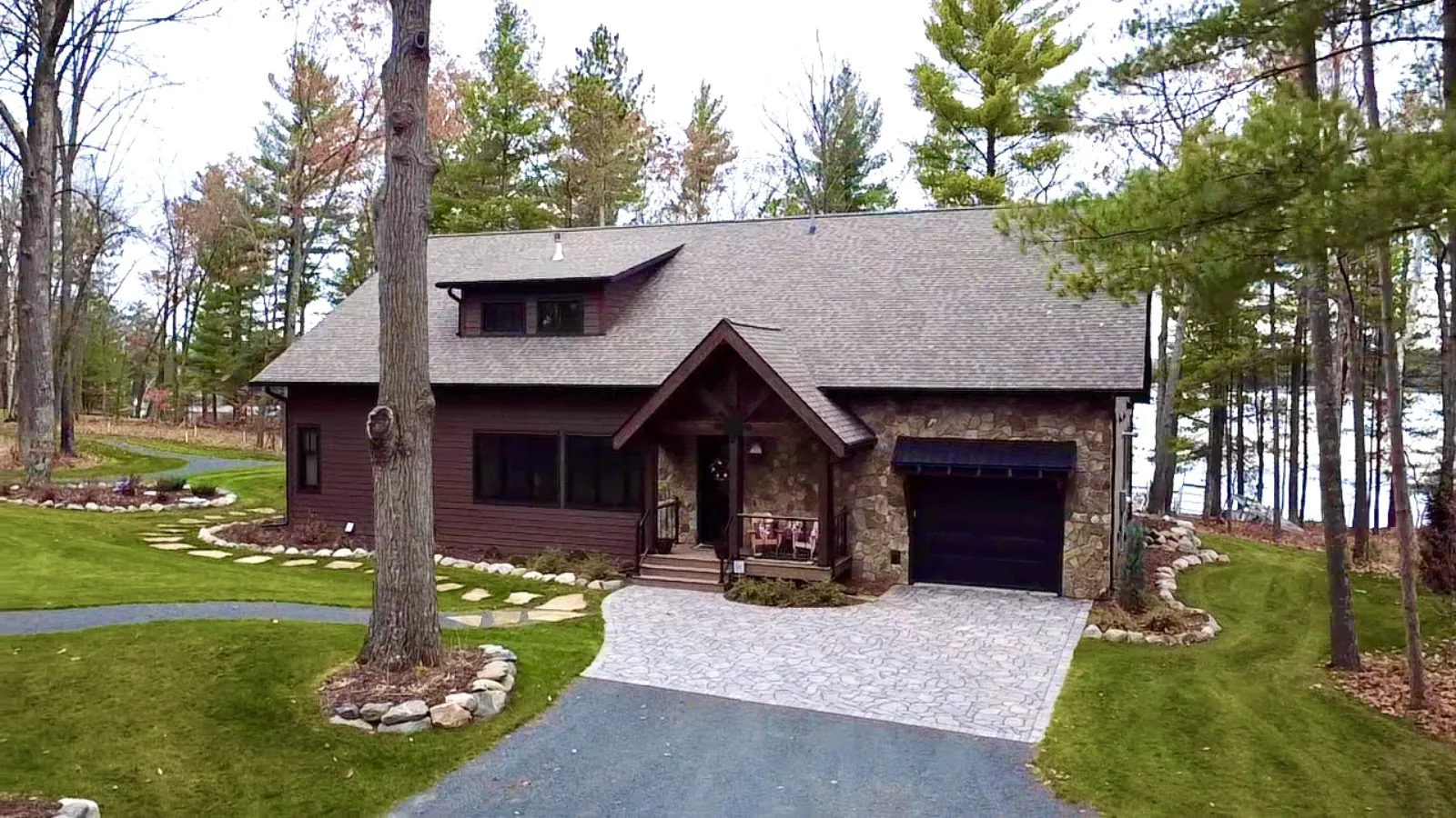 Exterior of a Northwoods lake home with brown siding, natural stone masonry and a timber-framed covered entry among pines.